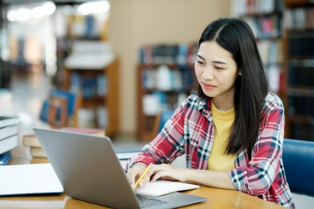 Young university student using laptop for online learning, searching and learning at library.